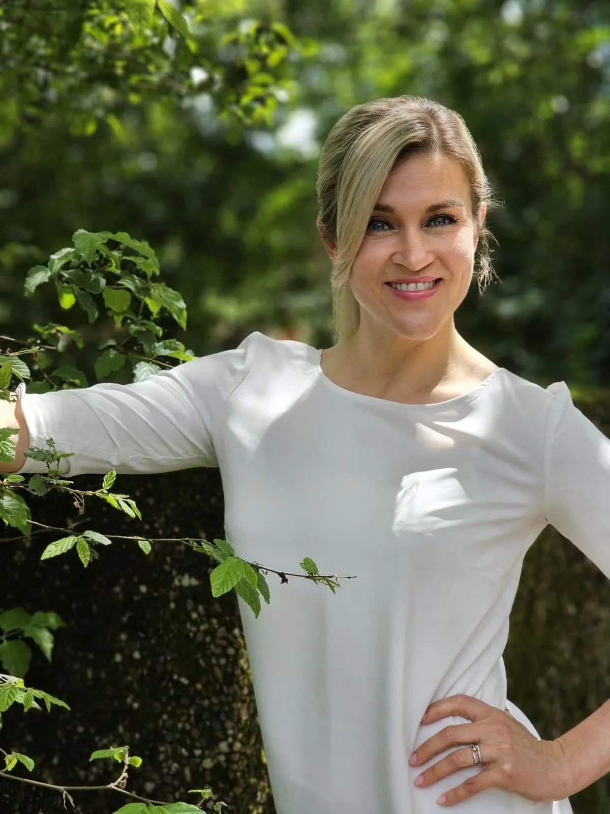 Natalie Leer in weißer Bluse an einem Baum, lächelnd